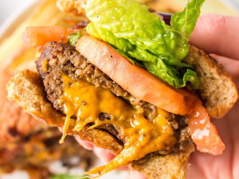 A bite taken out of a cheeseburger filled with lettuce and tomatoes.