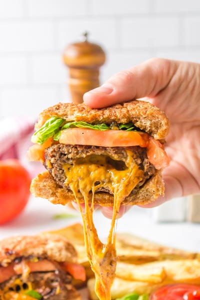 A juicy lucy burger filled with melted cheddar cheese that is oozing out of the burger.