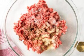 Ground beef topped with seasoning in a glass bowl.