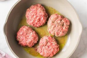 Four burger patties cooking in a skillet.