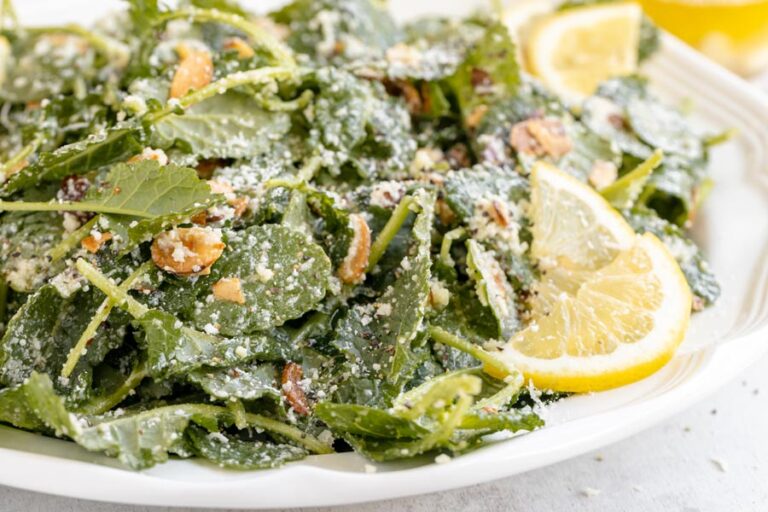 Baby kale salad on a plate topped with grated parmesan, toasted almonds and lemon slices.