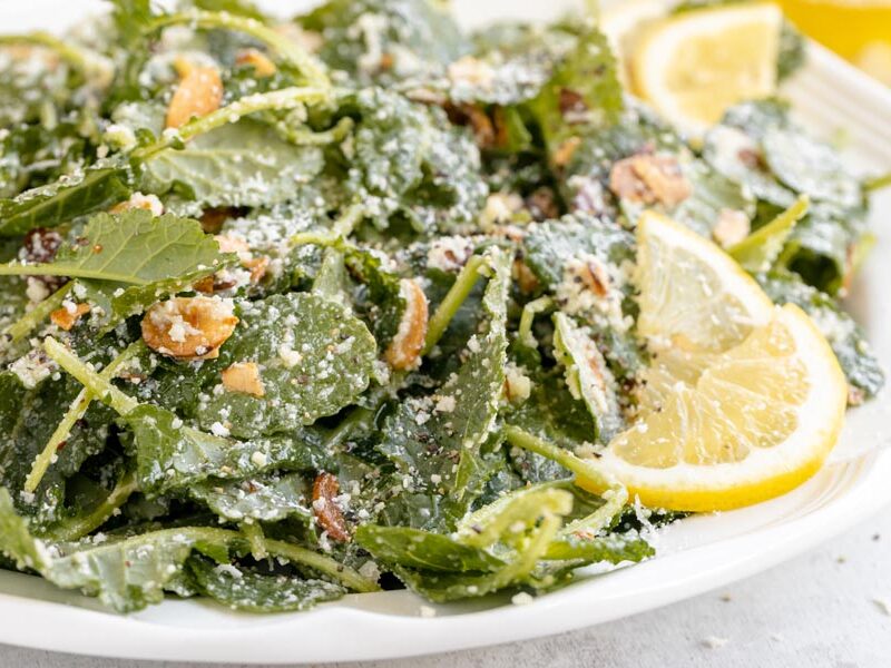 Baby kale salad on a plate topped with grated parmesan, toasted almonds and lemon slices.