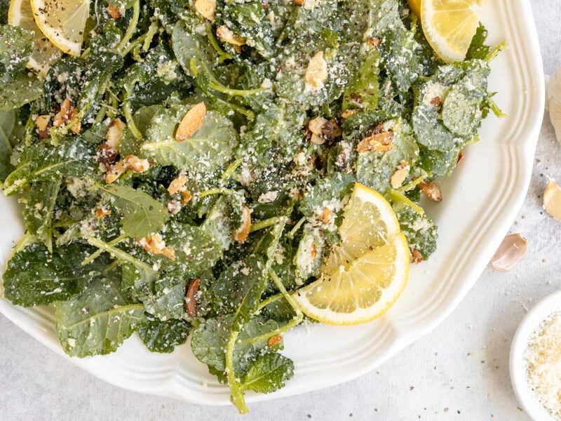 Kale salad with lemon, Parmesan and almonds on a platter, with garlic nearby.