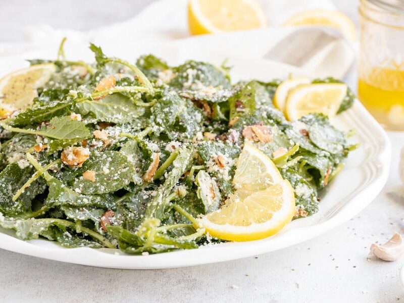Garlic kale salad on a platter with lemon vinaigrette dressing nearby and whole cloves of garlic.