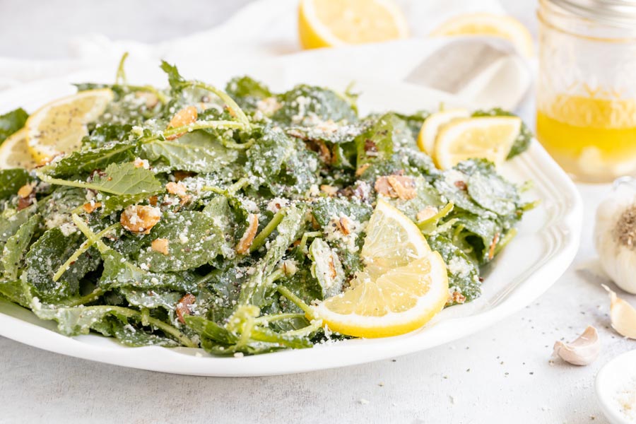 Garlic kale salad on a platter with lemon vinaigrette dressing nearby and whole cloves of garlic.