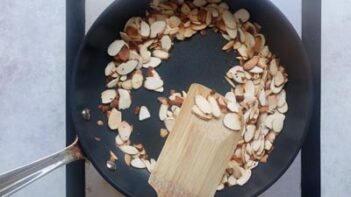 A non-stick skillet with toasted almonds and a spatula holding toasted almonds on it.