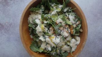 A large wooden bowl with kale leaves, almond and grated parmesan cheese scattered on top.