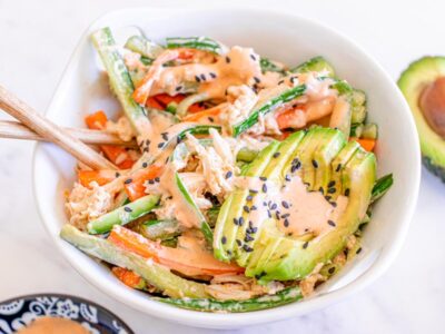 Creamy kani salad with shredded crab, cucumber, carrots, avocado, spicy mayo, and black sesame seeds served in a white bowl.