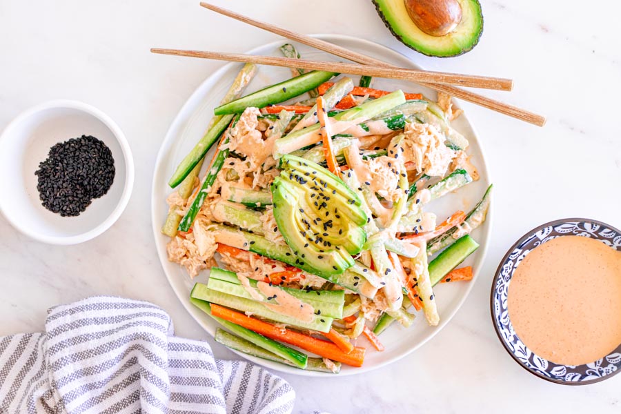 Overhead view of creamy kani salad topped with sliced avocado and black sesame seeds, with extra spicy mayo on the side.