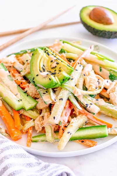 Close-up of kani salad with shredded crab, crisp cucumber and carrots, avocado, creamy spicy mayo, and black sesame seeds.