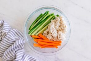 Shredded crab, julienned cucumber, and carrots arranged in a glass bowl to make kani salad.