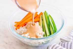 Creamy spicy mayo dressing being poured over shredded crab, cucumber, and carrots for kani salad.