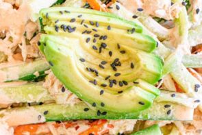 Close-up of sliced avocado topped with black sesame seeds over creamy kani salad.