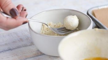 rolling a cheese ball into almond flour with a fork