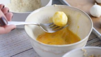 lifting up a goat cheese ball coated in egg wash with a fork