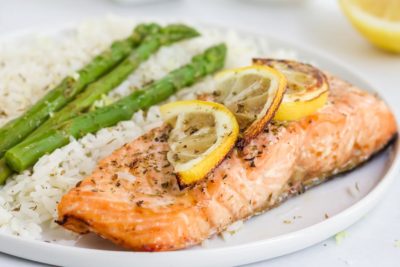 keto salmon on a plate next to cauliflower rice and green vegetables