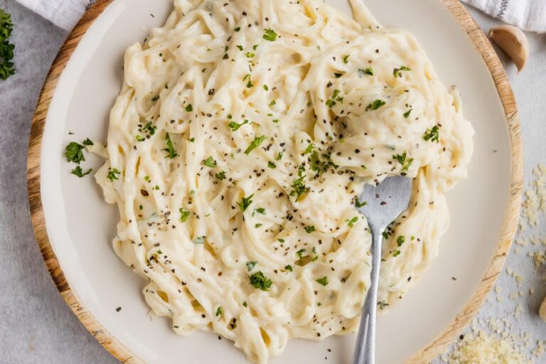 A plate of fettucine alfredo topped with pepper and parsley and a fork dug into the noodles.