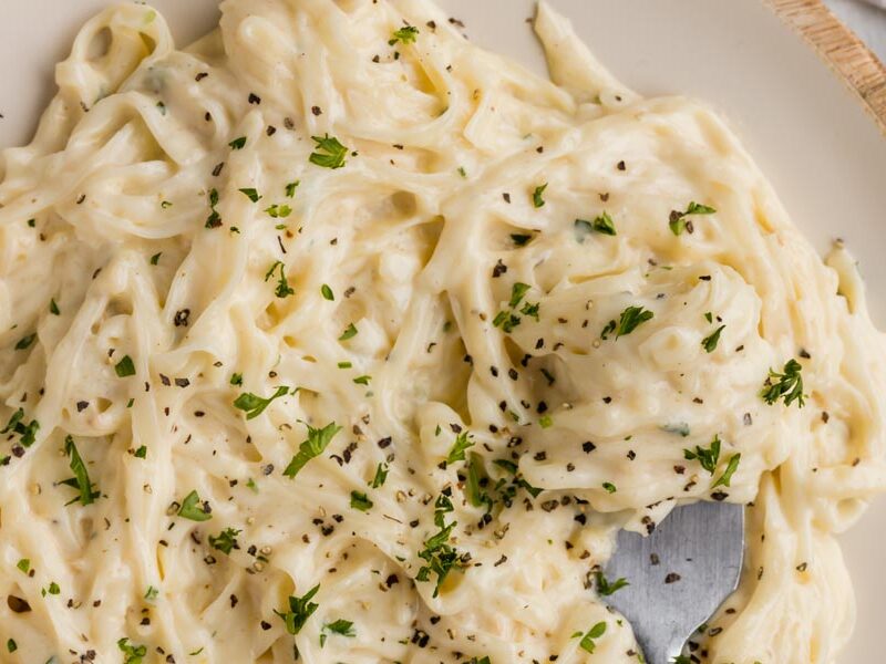 A fork sitting in a plate of creamy pasta.