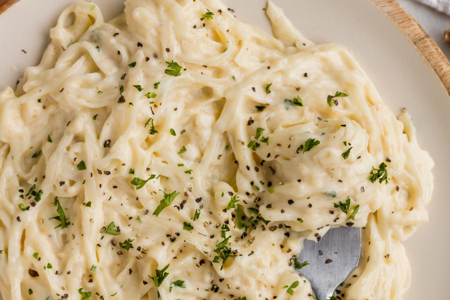 A fork sitting in a plate of creamy pasta.
