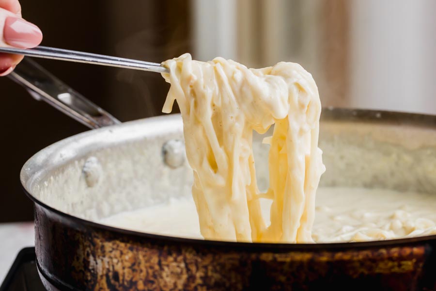 Holding a spoonful of creamy fettucine alfredo over a skillet.