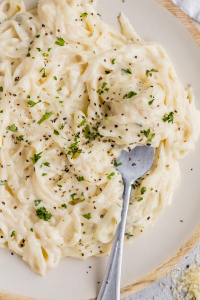A fork sitting in creamy fettucine topped with pepper and chopped parsley.