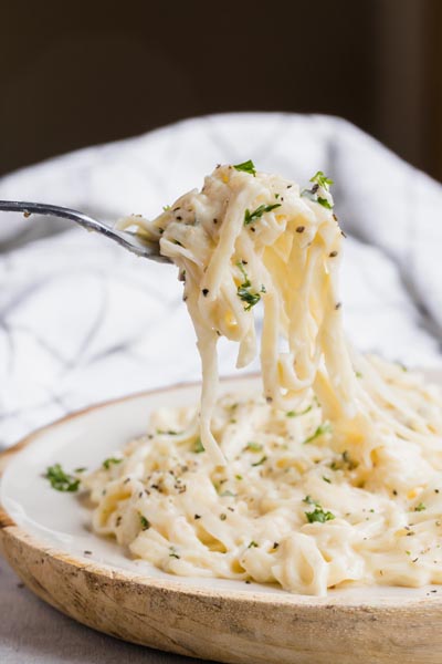 A fork holding noodles over a plate of rich creamy pasta.
