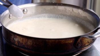 A large skillet with creamy white sauce inside.