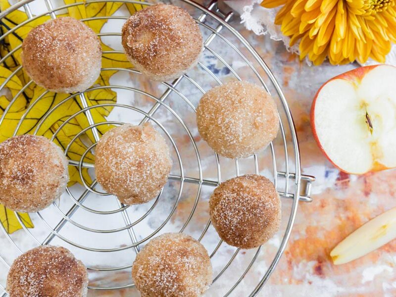 Overhead view of several keto donut bites arranged on a round cooling rack, surrounded by fall-themed decor and apple slices.