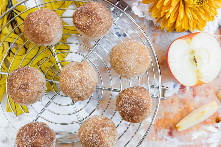 Overhead view of several keto donut bites arranged on a round cooling rack, surrounded by fall-themed decor and apple slices.