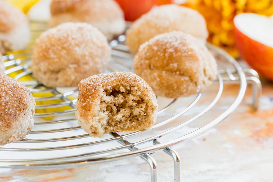 A bitten keto donut bite revealing its fluffy interior, placed on a cooling rack with whole donuts in the background.