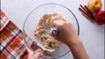 Hand using a whisk to combine ingredients in a glass bowl for keto apple cider donut bites.