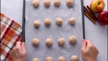 A parchment-lined baking sheet with evenly spaced raw keto donut bites ready for baking.