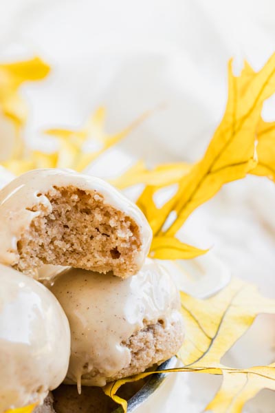 Glazed keto donut bites stacked with one cut open to show the moist inside, styled on top of yellow fall leaves.
