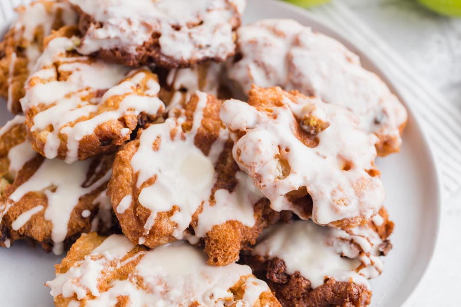 lots of apple fritter donuts on a plate with a white sugary glaze on top