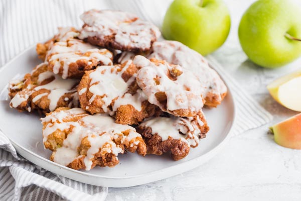 a plate full of apple fritters with glaze on top next to sliced apples