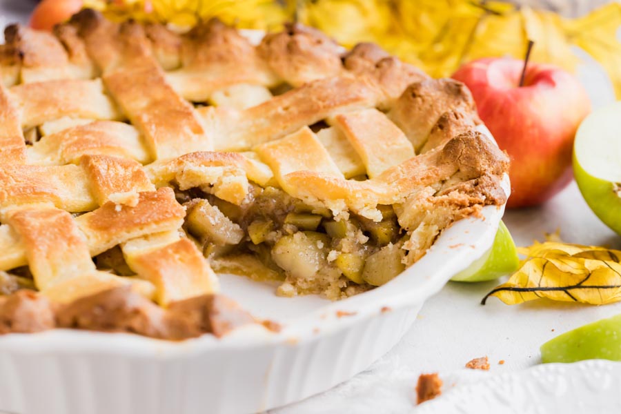 a slice out of a pie with apples and leaves in the background