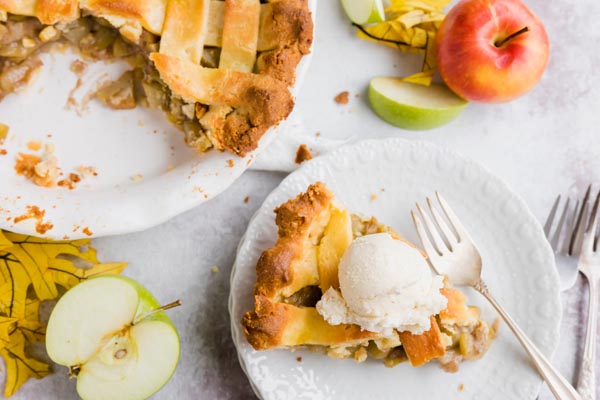 a slice of pie on a plate topped with vanilla ice cream and surrounded by apples