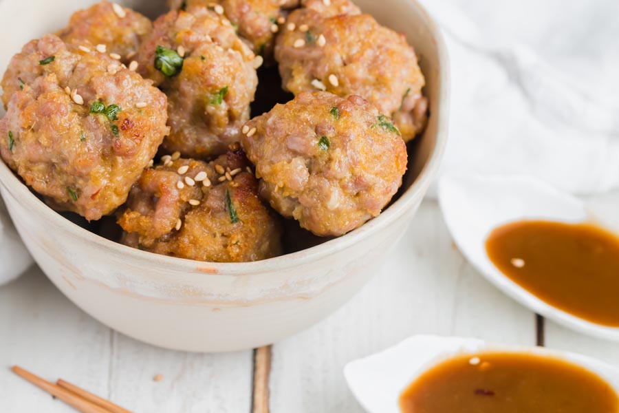 juicy low carb meatballs with sesame and ginger next to a dish of sauce
