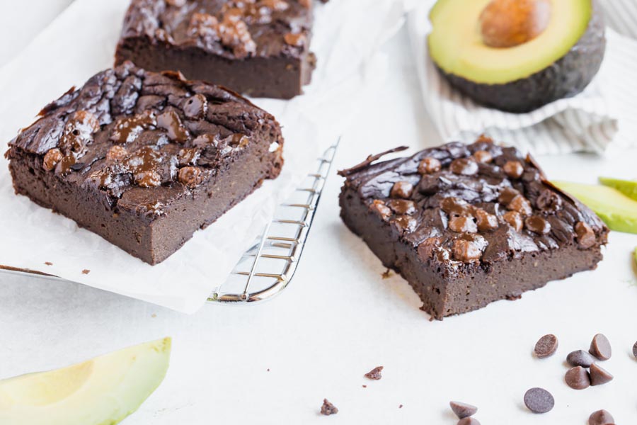 three brownies with one on a wire rack and an avocado near by