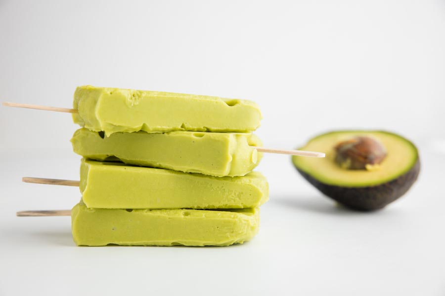 keto avocado popsicles in a stack with an avocado in the background