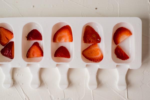 lining strawberry slices in a popsicle mold