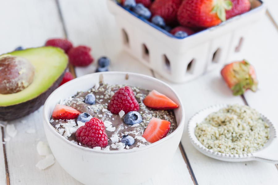 thick avocado bowl with berries and coconut on top and a basket of berries in the background