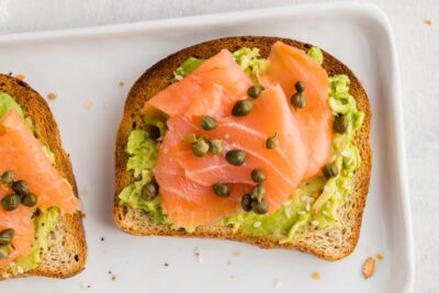 a piece of keto bread lightly toasted on a plate and topped with avocado, smoked salmon and capers