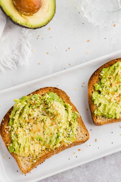 two slices of avocado toast on a plate and topped with everything bagel seasoning