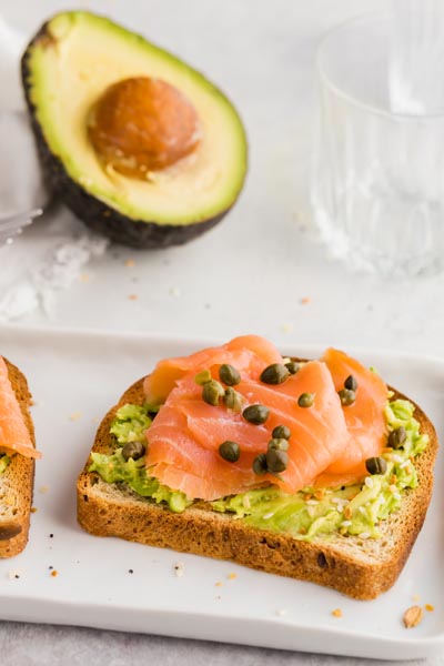 a half an avocado sits behind a breakfast plate with smoked salmon toast