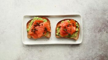 two slices of smoked salmon topped avocado toast on a plate