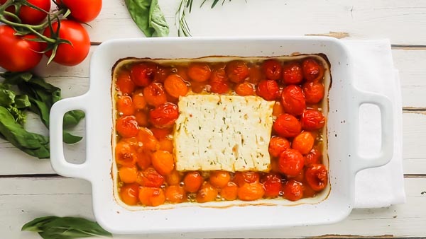 baked block of feta in the center of cooked tomatoes