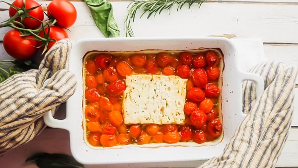 setting down a hot casserole dish with baked feta and tomatoes in it