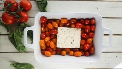 a block of feta cheese sitting in baking pan with tomatoes surrounding it