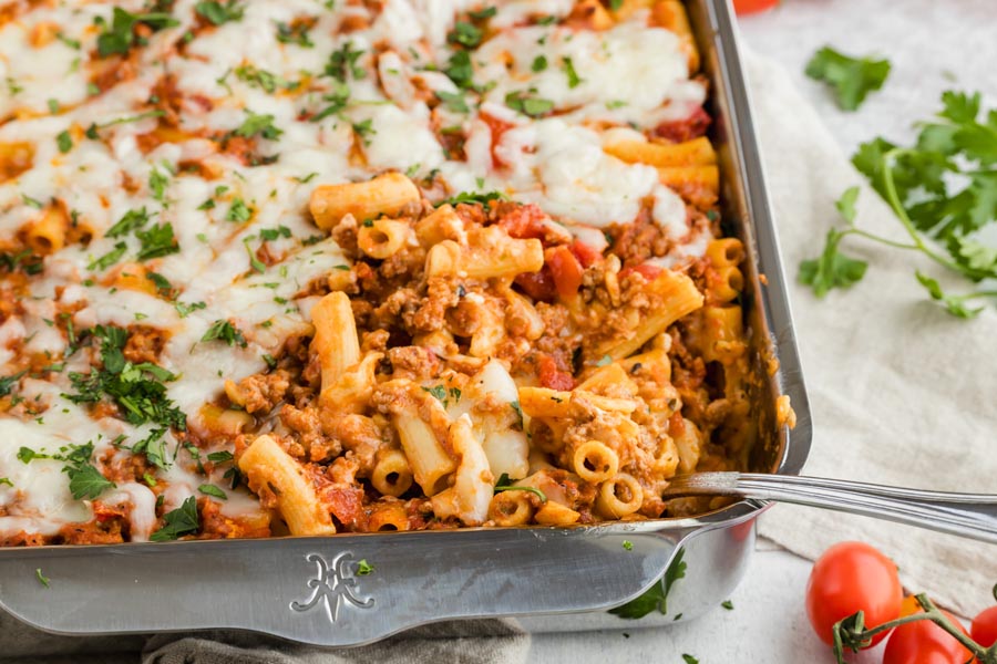 A spoon resting in a casserole dish filled with a beefy pasta casserole.